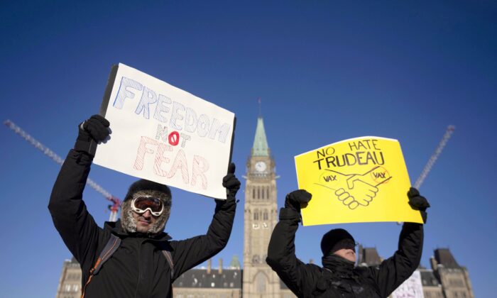 Protesters participating in a cross-country truck convoy protesting vaccine mandates and other restrictions hold signs on Parliament Hill in Ottawa on Jan. 29, 2022. (The Canadian Press/Adrian Wyld)