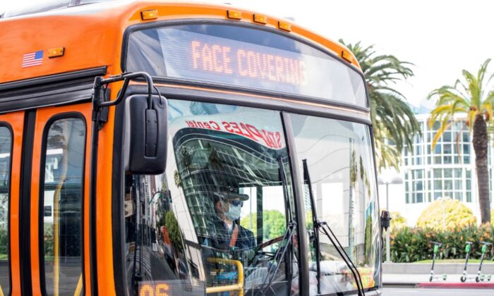 A man wearing a face mask drives a bus with a sign in the downtown area in Los Angeles, Calif., on March 8, 2021. (Valerie Macon/AFP via Getty Images)