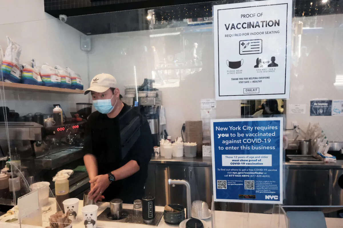An employee at a coffee shop in Manhattan wears a masks as signs ask for proof of vaccination, on the day that a mask mandate went into effect in New York on Dec. 13, 2021. (Spencer Platt/Getty Images)
