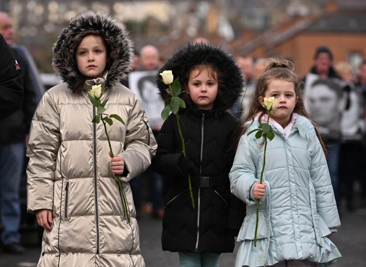 Three young family members hold flowers as they walk commemorating the victims during a Walk of Remembrance to Memorial Garden to mark the 50th Anniversary of Bloody Sunday in Londonderry, Northern Ireland, on Jan. 30, 2022. (Charles McQuillan/Getty Images)