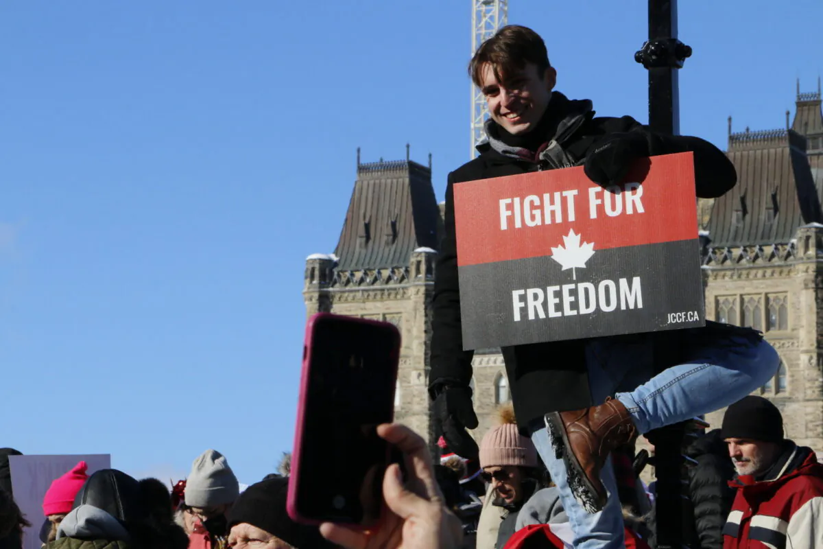 A protester hangs from a lamp post in front of Parliament Hill in Ottawa on Jan. 29, 2022. (Noé Chartier/The Epoch Times)