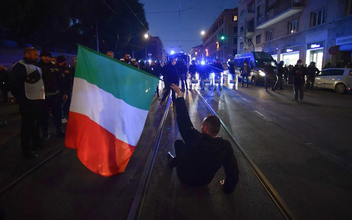 A protester holding the Italian flag sits in before anti-riot policemen during a demonstration against the new restrictions imposed by the so-called "Super Green Pass," near piazza San Giovanni in Rome on Jan. 15, 2022. (Filippo Monteforte/AFP via Getty Images)