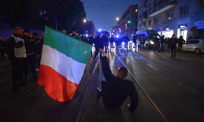 A protester holding the Italian flag sits in before anti-riot policemen during a demonstration against the new restrictions imposed by the so-called "Super Green Pass," near piazza San Giovanni in Rome on Jan. 15, 2022. (Filippo Monteforte/AFP via Getty Images)