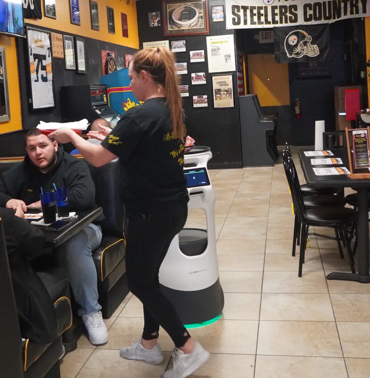 Meghan Wollerman takes food from Champ the robot and serves patrons Lelulo's Pizzara Cape Coral, Fla. Jan. 18, 2022. (Photo: Jann Falkenstern, The Epoch Times)