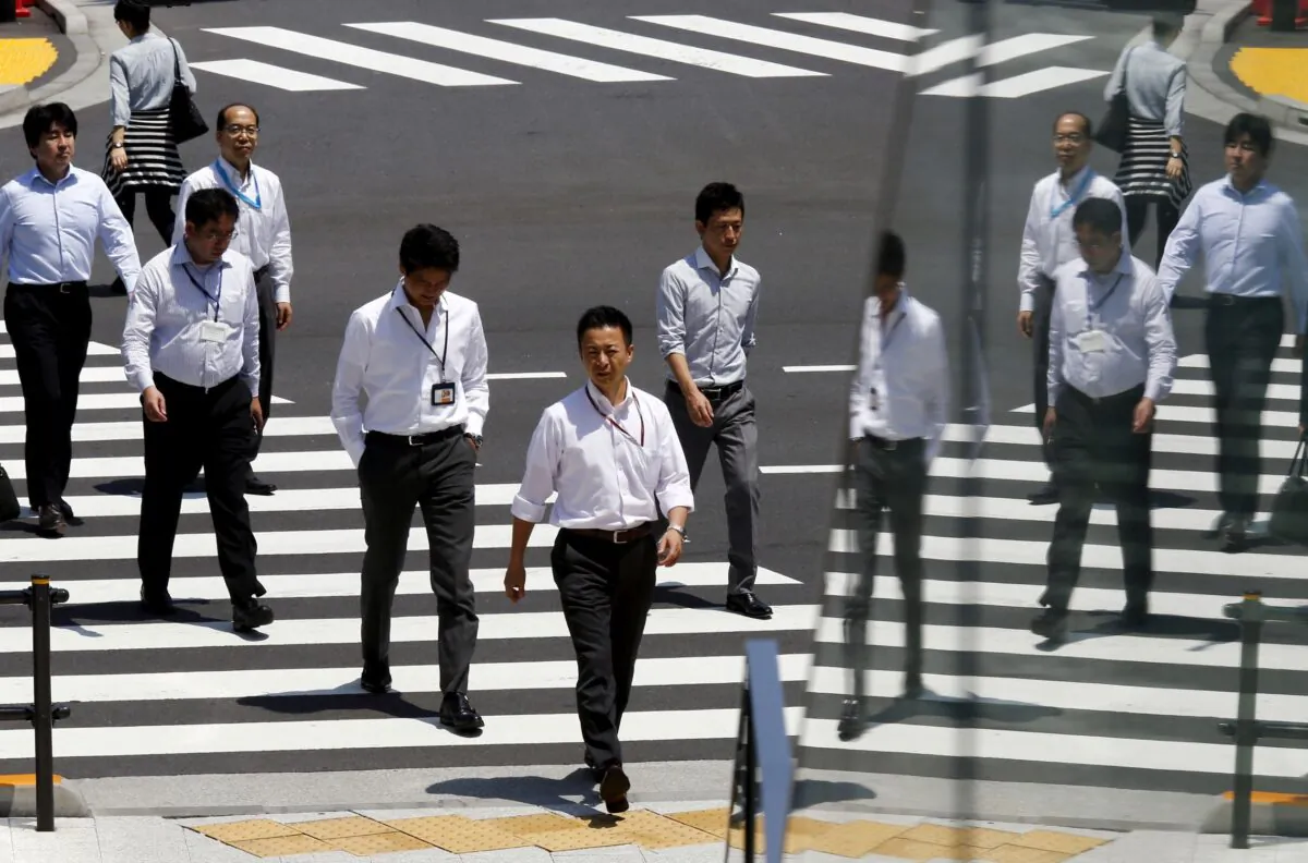 Office workers are reflected in a glass railing as they cross a street during lunch hour in Tokyo, Japan, on June 1, 2015. (Thomas Peter/Reuters)