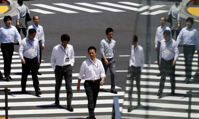 Office workers are reflected in a glass railing as they cross a street during lunch hour in Tokyo, Japan, on June 1, 2015. (Thomas Peter/Reuters)