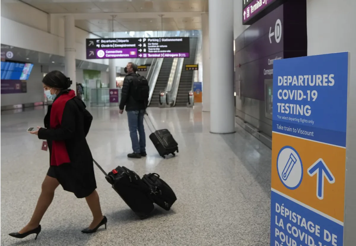 People walk past a COVID-19 testing sign at Toronto Pearson International Airport, on Dec. 3, 2021.
(The Canadian Press/Nathan Denette)