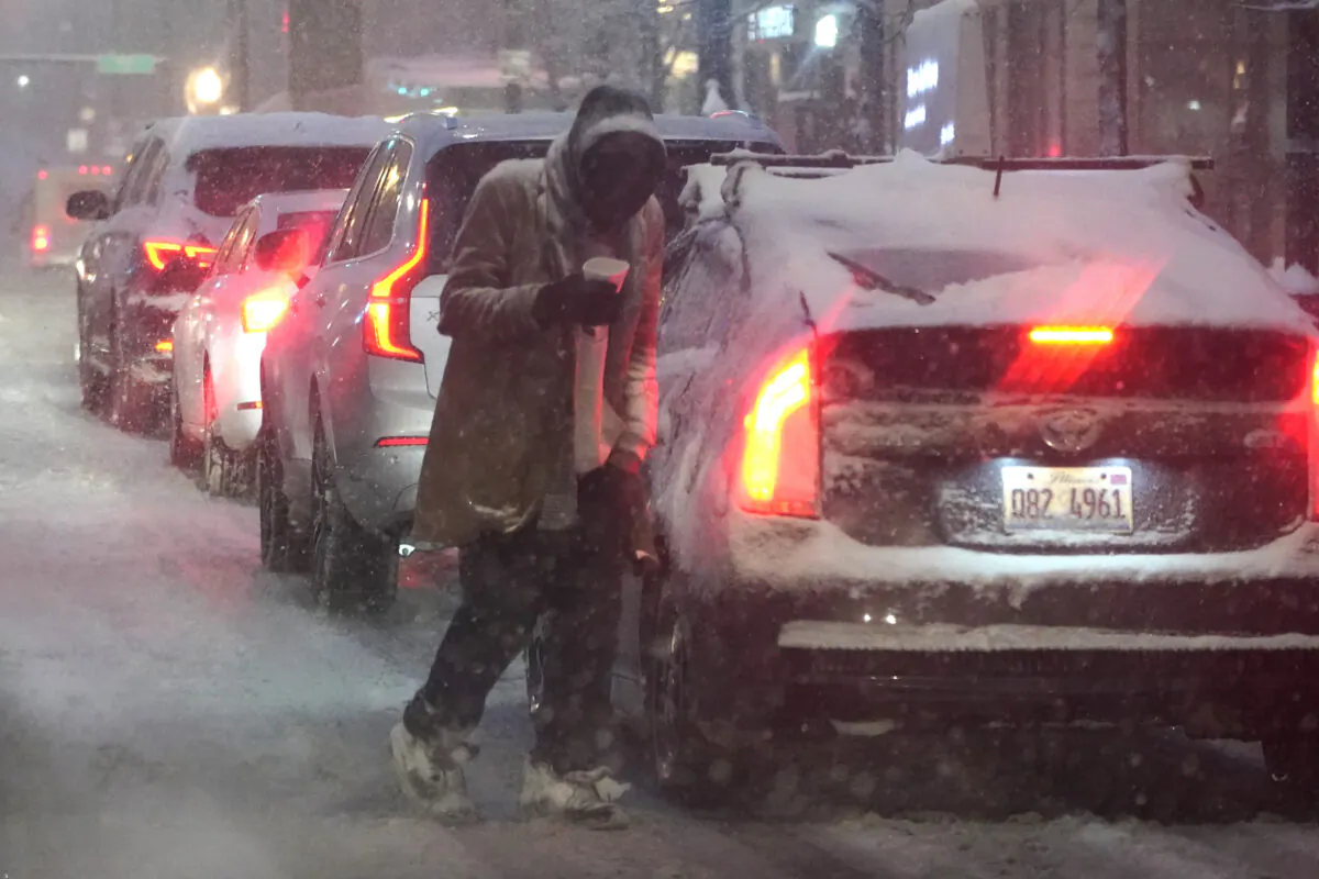 A panhandler walks between cars as he navigates windy, falling snow and slushy street conditions in Chicago on Feb. 2, 2022. (Charles Rex Arbogast/AP Photo)