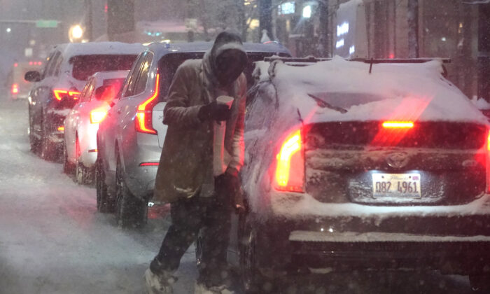 A panhandler walks between cars as he navigates windy, falling snow and slushy street conditions in Chicago on Feb. 2, 2022. (Charles Rex Arbogast/AP Photo)