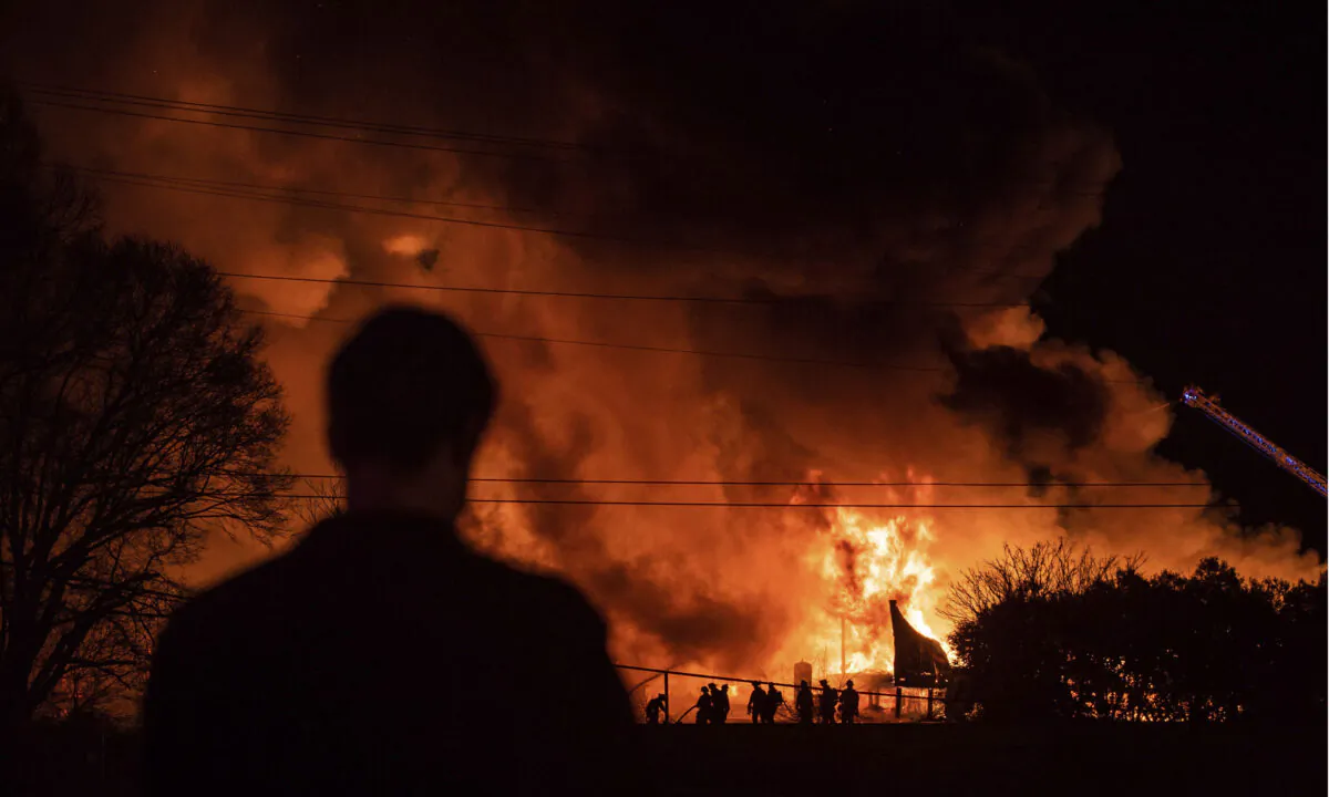 A bystander watches as Winston-Salem firefighters battle a structure fire at Weaver Fertilizer Co. in Winston-Salem, N.C., on Jan. 31, 2022. (Allison Lee Isley/The Winston-Salem Journal via AP)