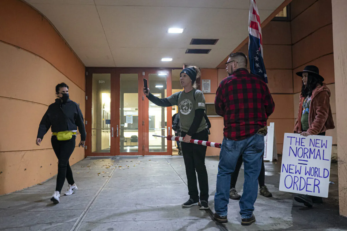 A masked attendee walks past anti-vaccine mandate protesters as they gather during a Portland Public Schools board meeting to discuss a proposed vaccine mandate for students in Portland, Ore., on Oct. 26, 2021. (Nathan Howard/Getty Images)