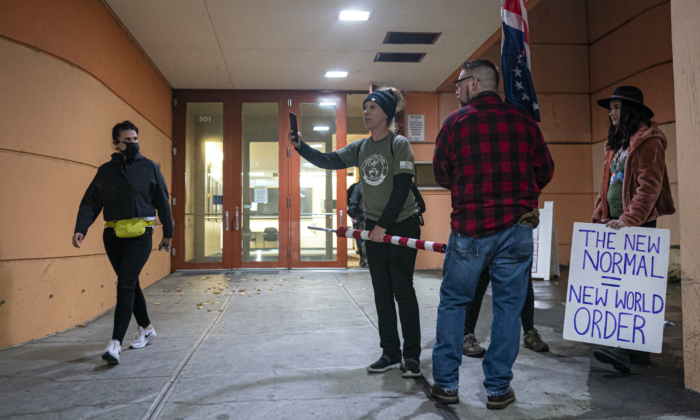 A masked attendee walks past anti-vaccine mandate protesters as they gather during a Portland Public Schools board meeting to discuss a proposed vaccine mandate for students in Portland, Ore., on Oct. 26, 2021. (Nathan Howard/Getty Images)