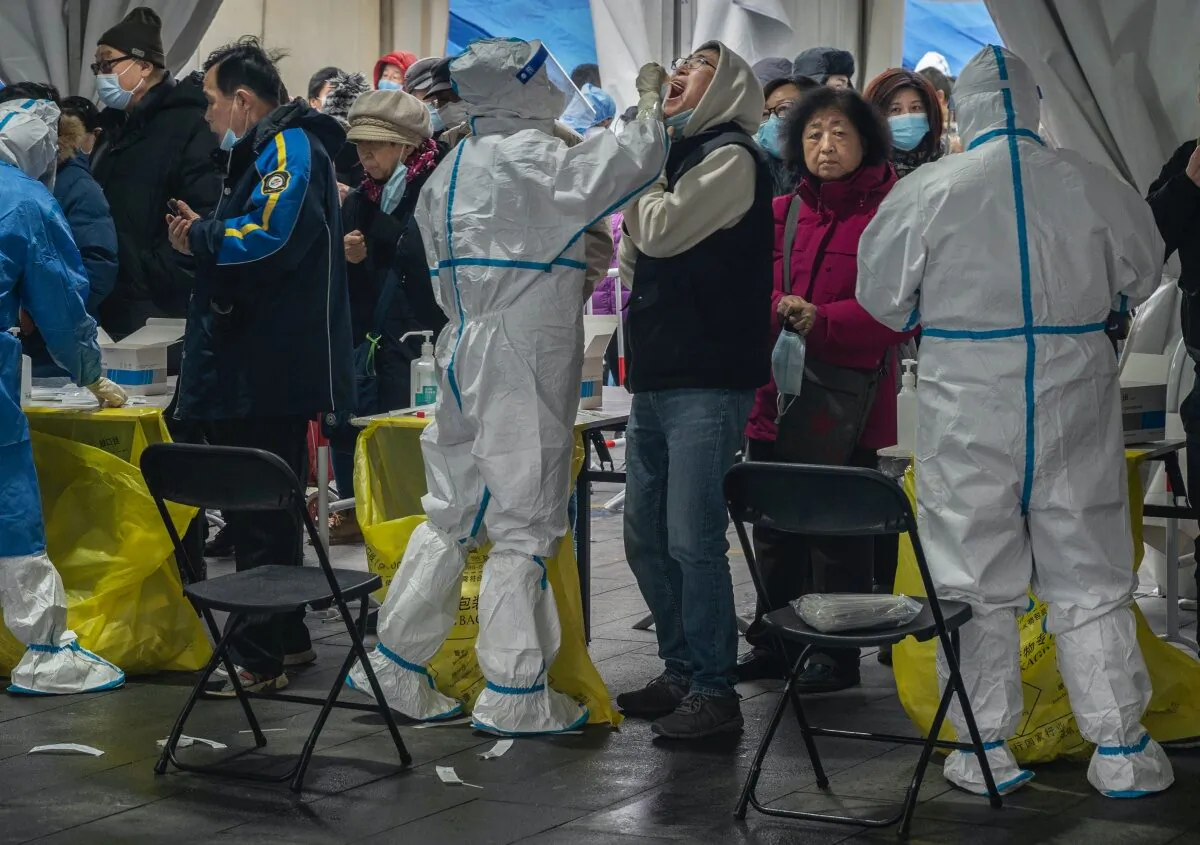 A health worker in protective gear takes a swab from a man for a nucleic acid test to detect COVID-19 as others line up at a mass testing site on Jan. 24, 2022 in Beijing, China.  (Kevin Frayer/Getty Images)