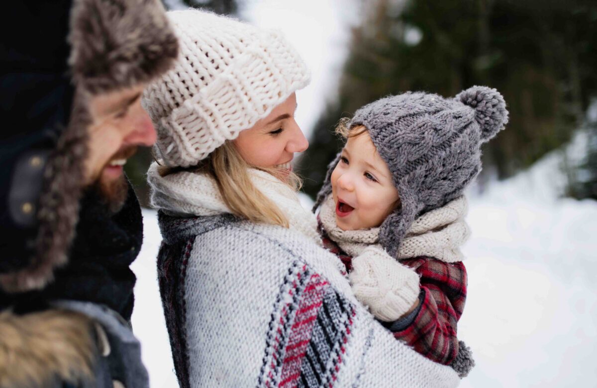 Father and mother with small child in winter nature, standing in the snow. (Halfpoint/Shutterstock)