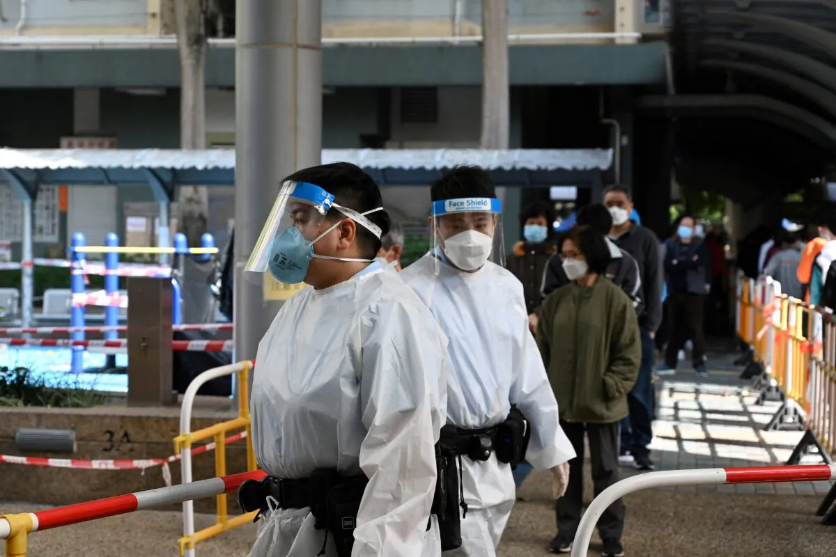 Police (C) in full protective clothing stand guard whilst residents (behind) queue up  for Covid tests following a recent cluster of coronavirus cases, at the Kwai Chung housing estate in Hong Kong on January 27, 2022. (Photo by Peter Parks / AFP via Getty Images)