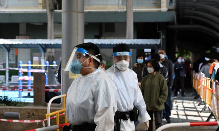Police (C) in full protective clothing stand guard whilst residents (behind) queue up  for Covid tests following a recent cluster of coronavirus cases, at the Kwai Chung housing estate in Hong Kong on January 27, 2022. (Photo by Peter Parks / AFP via Getty Images)