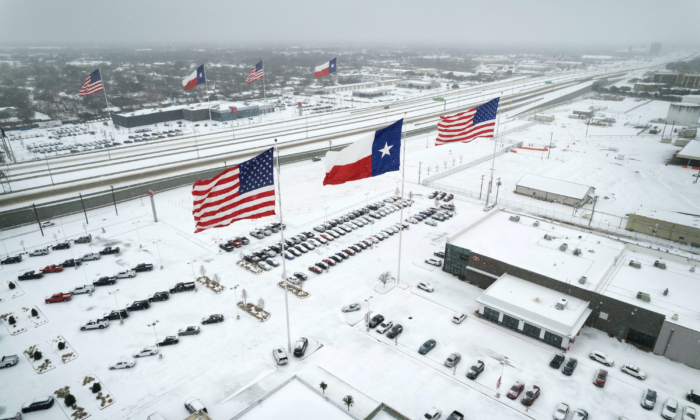 In an aerial view, U.S. and Texas state flags fly over car dealerships as light traffic moves through snow and ice on U.S. Route 183 on Feb. 3, 2022, in Irving, Texas. (John Moore/Getty Images)