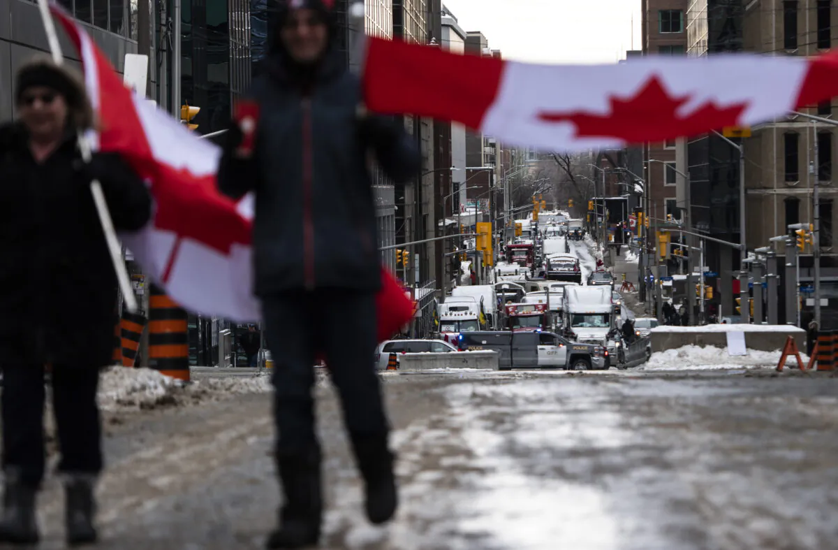 People carry Canadian flags as they walk toward Parliament Hill during the “Freedom Convoy” protest against COVID-19 mandates and restrictions, in Ottawa on Feb. 6, 2022. (The Canadian Press/Justin Tang)