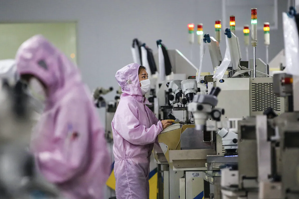 Chinese employees wearing protective masks and suits work on a smart chip production line in Sihong in China's eastern Jiangsu Province on February 16, 2020.  (STR / AFP)