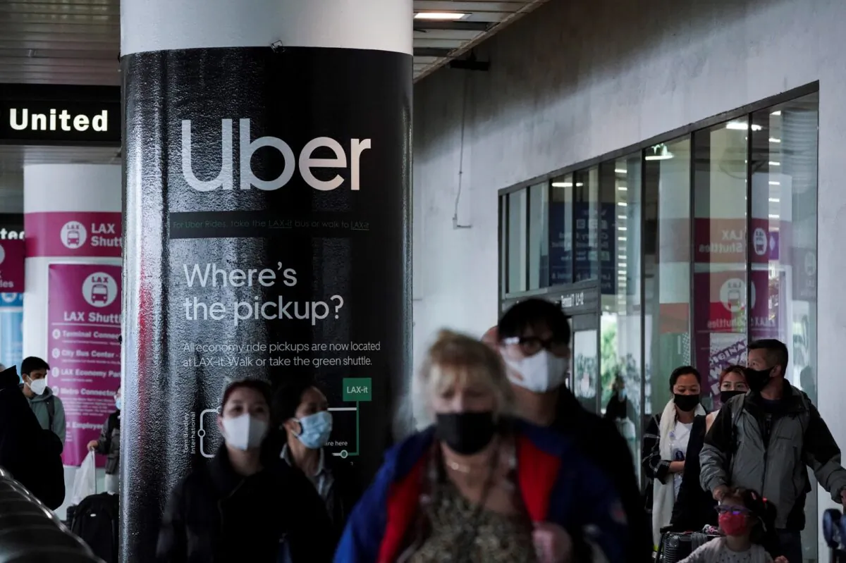 An Uber advertisement is seen behind travelers exiting the baggage claim area at the United Airlines terminal at Los Angeles International Airport (LAX), on Dec. 22, 2021. (Bing Guan/Reuters)