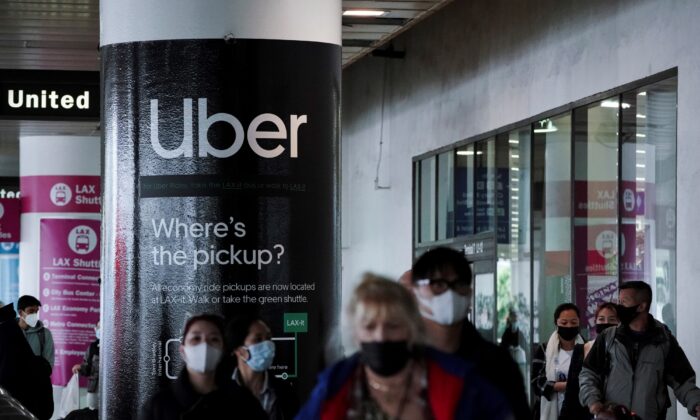 An Uber advertisement is seen behind travelers exiting the baggage claim area at the United Airlines terminal at Los Angeles International Airport (LAX), on Dec. 22, 2021. (Bing Guan/Reuters)