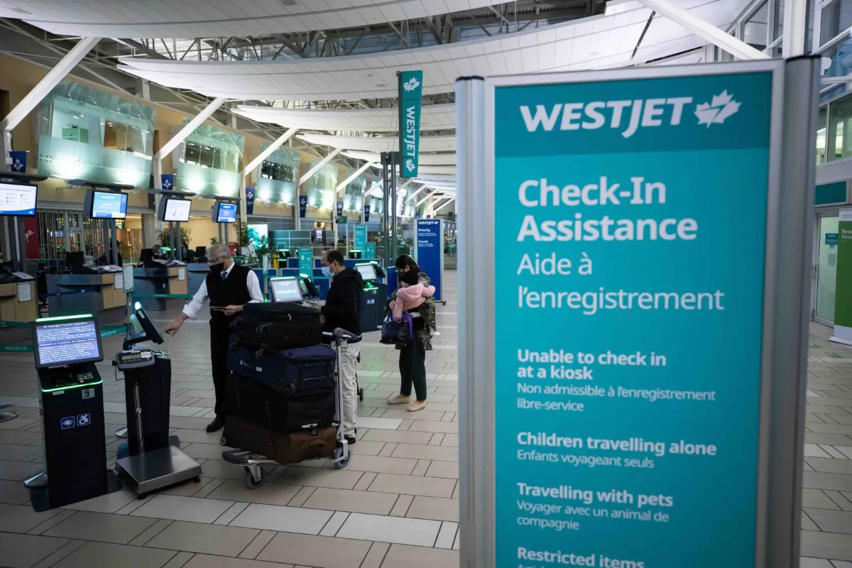 A Westjet employee assists people checking in for a domestic flight at Vancouver International Airport, in Richmond, B.C., on Jan. 21, 2021. (The Canadian Press/Darryl Dyck)