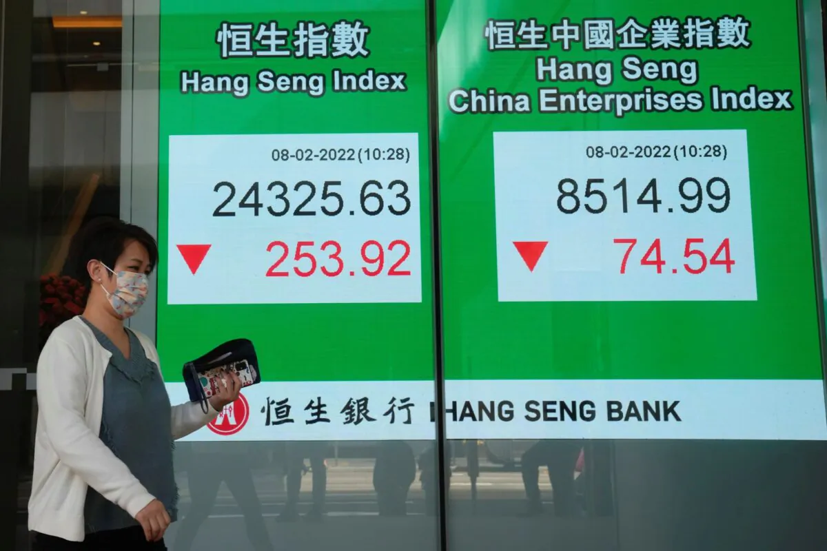 A woman wearing a face mask walks past a bank's electronic board showing the Hong Kong share index in Hong Kong, on Feb. 8, 2022. (Kin Cheung/AP Photo)