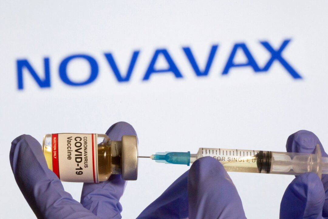 A woman holds a small bottle labeled with a "Coronavirus COVID-19 Vaccine" sticker and a medical syringe in front of displayed Novavax logo in this illustration taken on Oct. 30, 2020. (Dado Ruvic/Reuters)