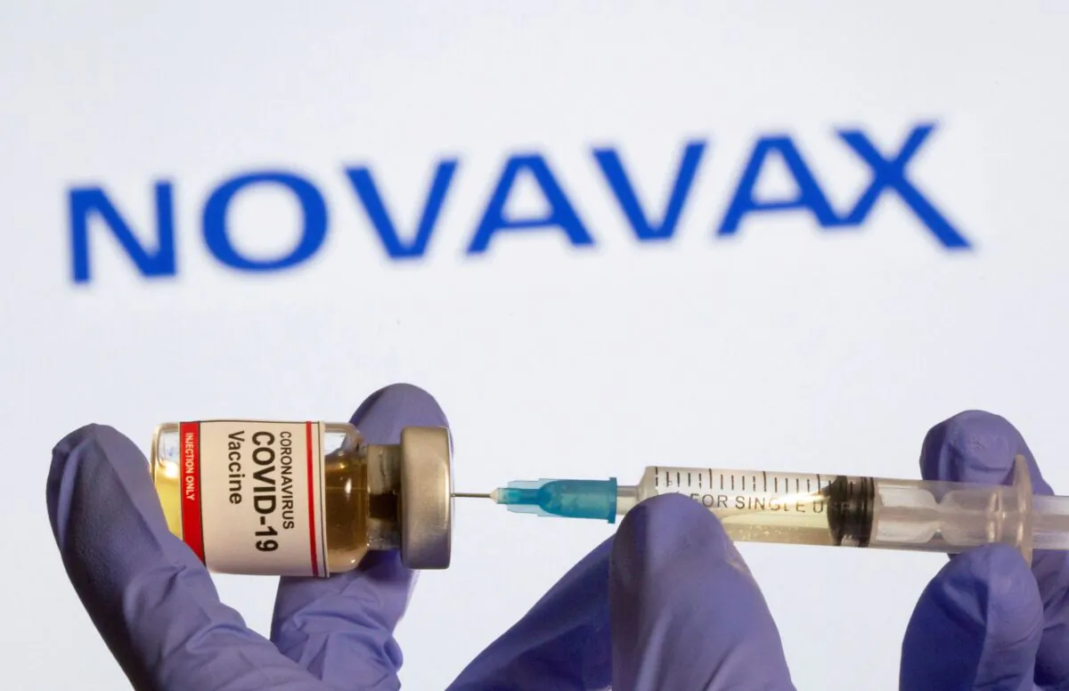 A woman holds a small bottle labeled with a "Coronavirus COVID-19 Vaccine" sticker and a medical syringe in front of displayed Novavax logo in this illustration taken, on Oct. 30, 2020. (Dado Ruvic/Reuters)