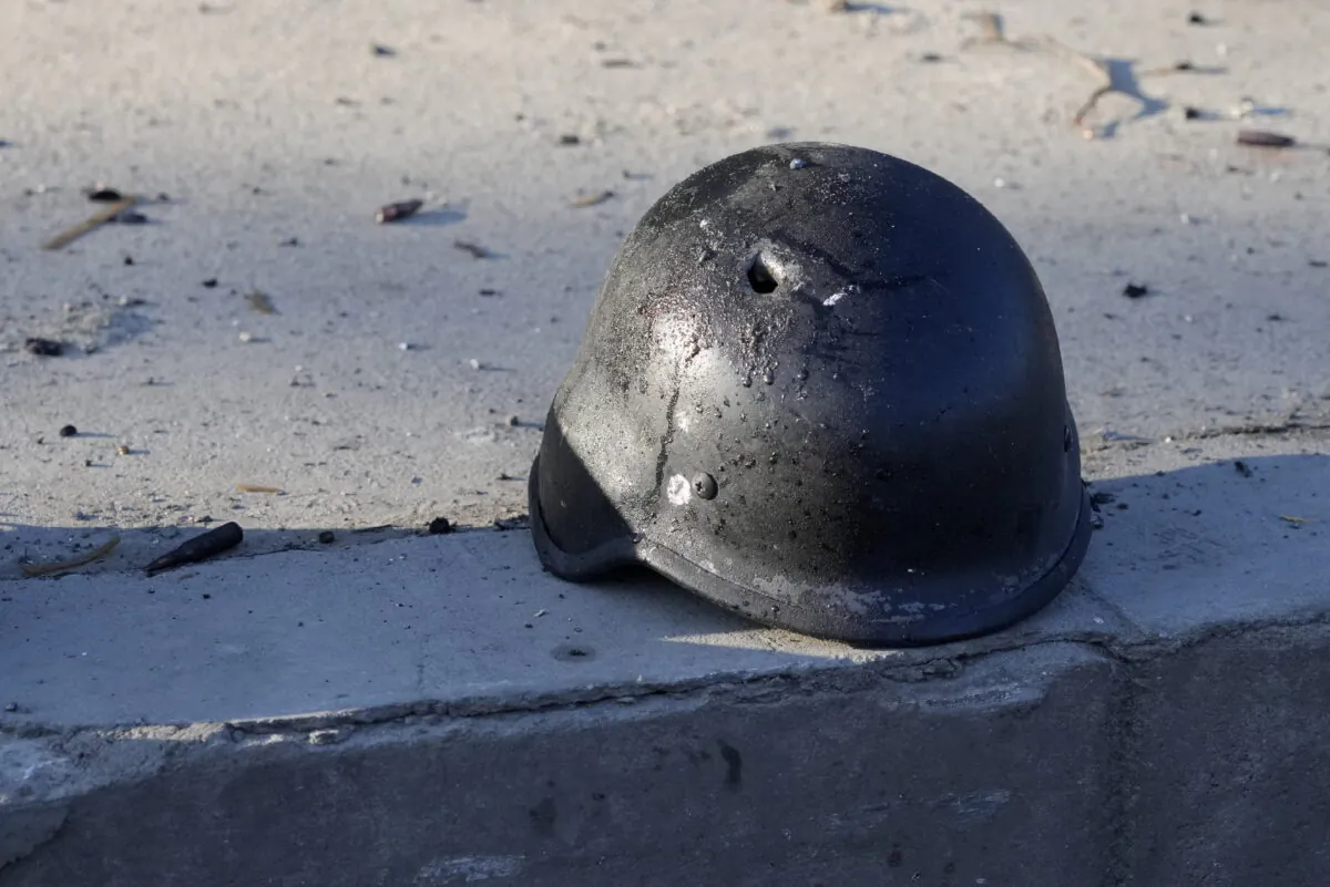 A soldier's helmet with a bullet hole near debris of burning military trucks, in a street in Kyiv, Ukraine, Saturday, Feb. 26, 2022. Russian troops stormed toward Ukraine's capital Saturday, and street fighting broke out as city officials urged residents to take shelter. (AP Photo/Efrem Lukatsky)