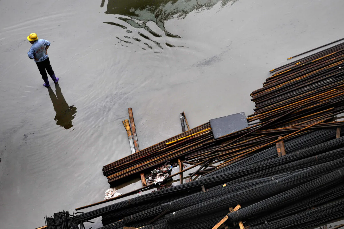 A Chinese worker stands in a large puddle of rain water next to iron rods at a construction site in Shanghai on Aug. 17, 2009. (Philippe Lopez/AFP via Getty Images)