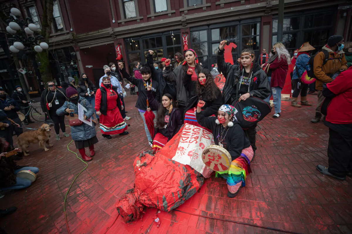 Women raise their fists while posing for a photograph after the Gassy Jack statue was toppled and covered in red paint during the annual Women's Memorial March in Vancouver on Feb. 14, 2022. (Darryl Dyck/The Canadian Press)