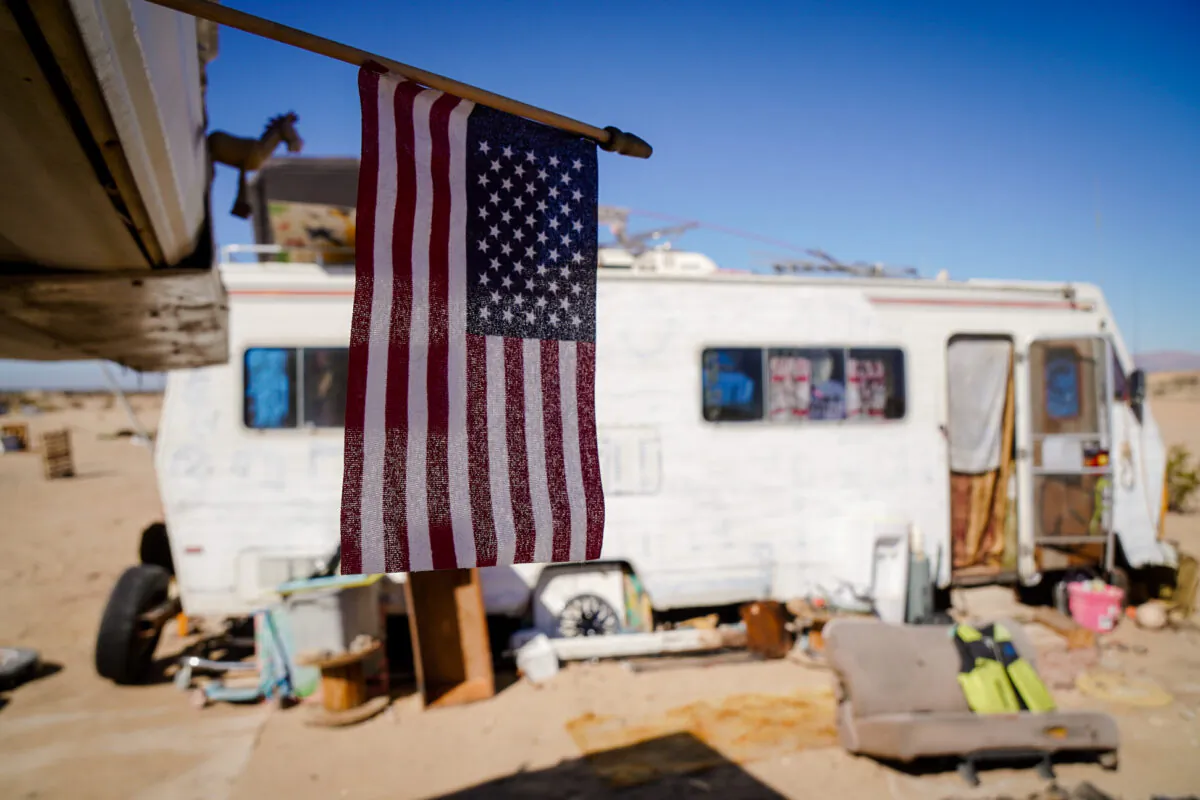 A flag stands vigil outside an old recreational vehicle, one of many that populate the nomadic lifestyle community known as "Slab City" outside of Niland, Calif., on Feb. 13, 2022. (Allan Stein/The Epoch Times)