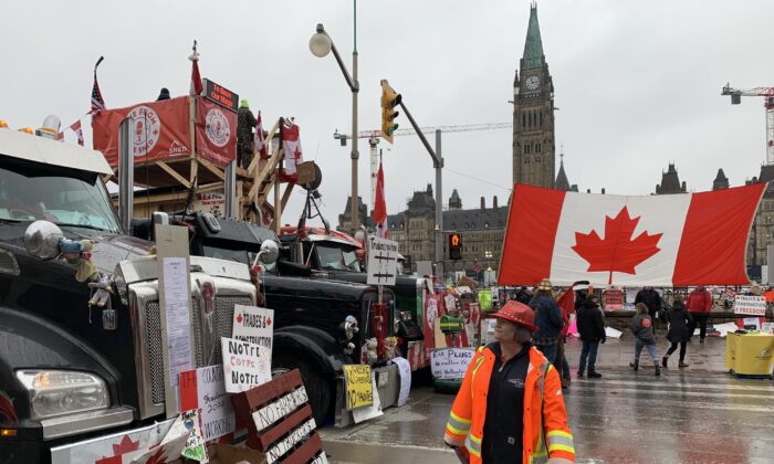 A woman reads the signboards placed by Freedom Convoy protesters outside Parliament Hill in Ottawa on Feb. 17, 2022 (Jonathan Ren/The Epoch Times)