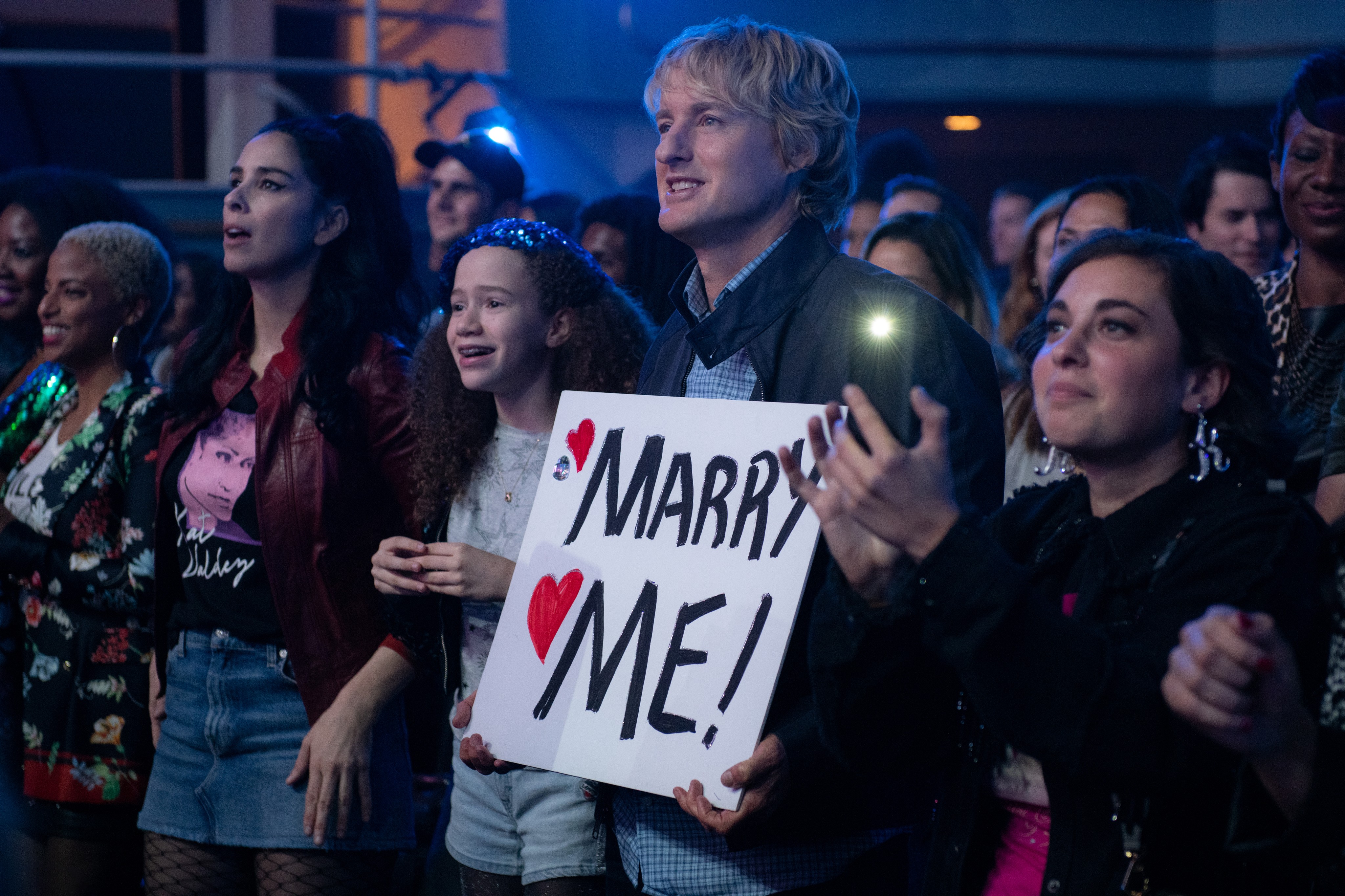 man holds sign in crowd in Marry Me