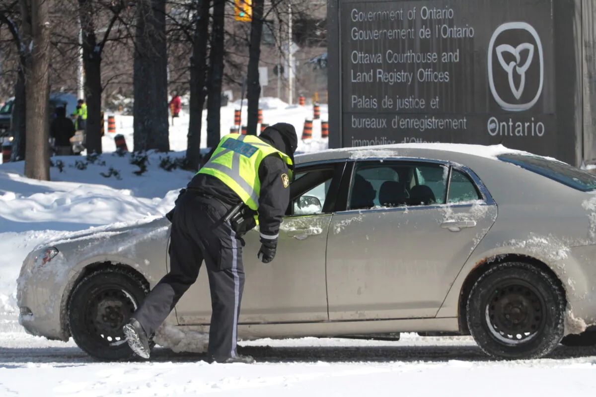 A police officer checks if a driver is exempt from a ban on people entering Ottawa's central area on Feb. 18, 2022 during the Freedom Convoy protest. (Richard Moore/The Epoch Times)