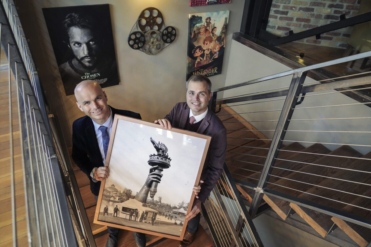Jeffrey (L) and Neal Harmon hold a photo of the Statue of Liberty's arm and torch as displayed at the 1876 Centennial Exhibition in Philadelphia. The brothers are inspired by the story of how newspaper publisher Joseph Pulitzer successfully held a fundraising campaign to bring the statue to New York City. (George Frey for American Essence)