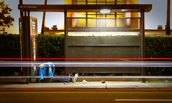 Cars drive past a sleeping homeless man inside an LA Metro bus stop in Los Angeles, Calif., on May 8, 2013. (John Fredricks/The Epoch Times)