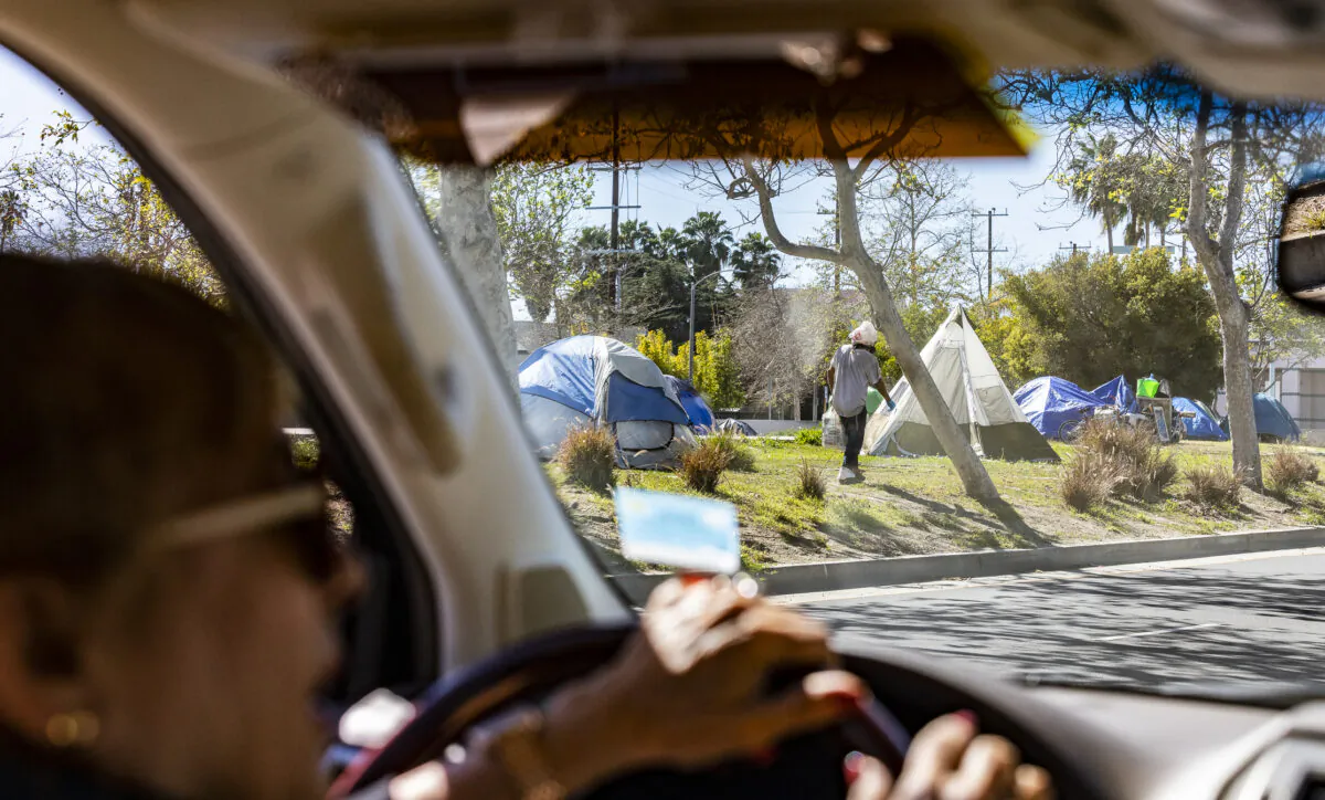 A Venice Beach resident drives past a homeless encampment in front of the Abbot Kinney Memorial Branch Library in Venice, Calif., on Feb. 18, 2022. (John Fredricks/The Epoch Times)