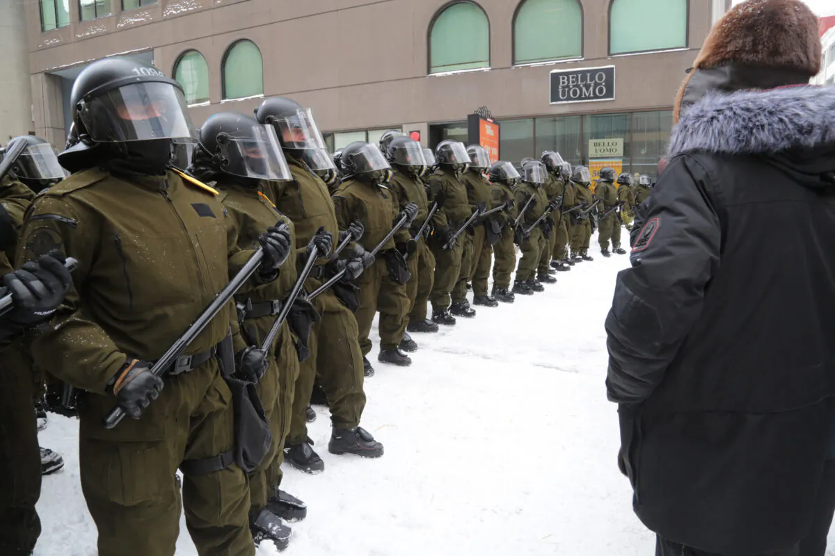 Protesters stare at police in helmets and carrying long batons near Parliament Hill in the Canadian capital of Ottawa on Feb. 20, 2022. (Richard Moore/The Epoch Times)
