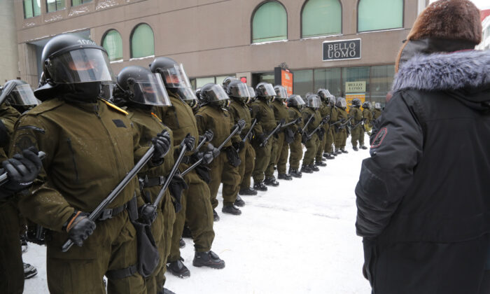 Protesters stare at police in helmets and carrying long batons near Parliament Hill in the Canadian capital of Ottawa on Feb. 20, 2022. (Richard Moore/The Epoch Times)
