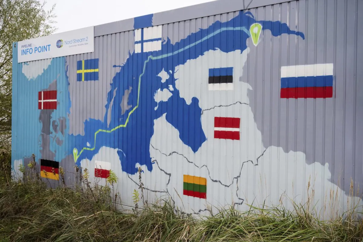 A sign reading "Nord Stream 2 Committed. Reliable. Safe." hangs above a painted map of the Nord Stream 2 pipeline from Russia to Germany at the natural gas receiving station in the Lubmin industrial estate in Lubmin, Germany, on Nov. 16, 2021. (Stefan Sauer/DPA via AP)