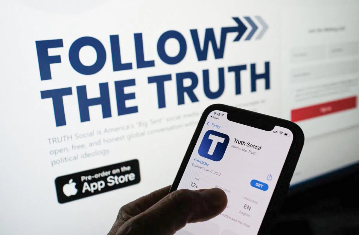 A person checks the app store on a smartphone for "Truth Social"—owned by Trump Media & Technology Group—with its website on a computer screen in the background, in Los Angeles, Calif., on Oct. 20, 2021. (Chris Delmas/AFP via Getty Images)