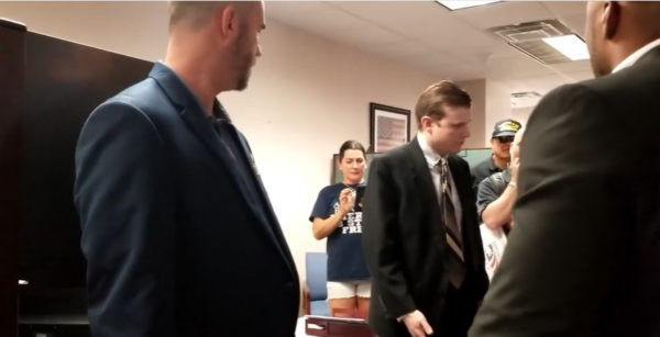 Screenshot from video showing the Aide to Florida State Rep. Chuck Brannan, surrounded by gun rights activists who want to know why he threw their petitions in the trash.