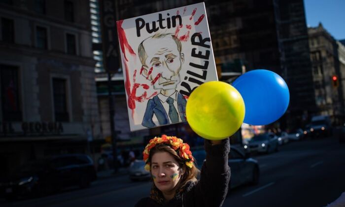 A woman holds a sign with a caricature of Russian President Vladimir Putin during a rally in support of the people of Ukraine in Vancouver, on Feb.24, 2022. (The Canadian Press/Darryl Dyck)
