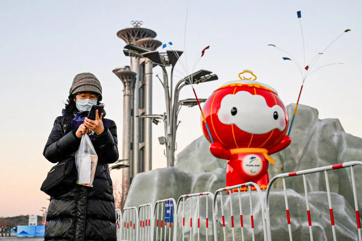 A woman checks her phone in front of an installation of Shuey Rhon Rhon, mascot of the Beijing 2022 Winter Paralympic Games at the Olympic Park in Beijing on Jan. 13, 2022.  (Jade Gao/AFP via Getty Images)