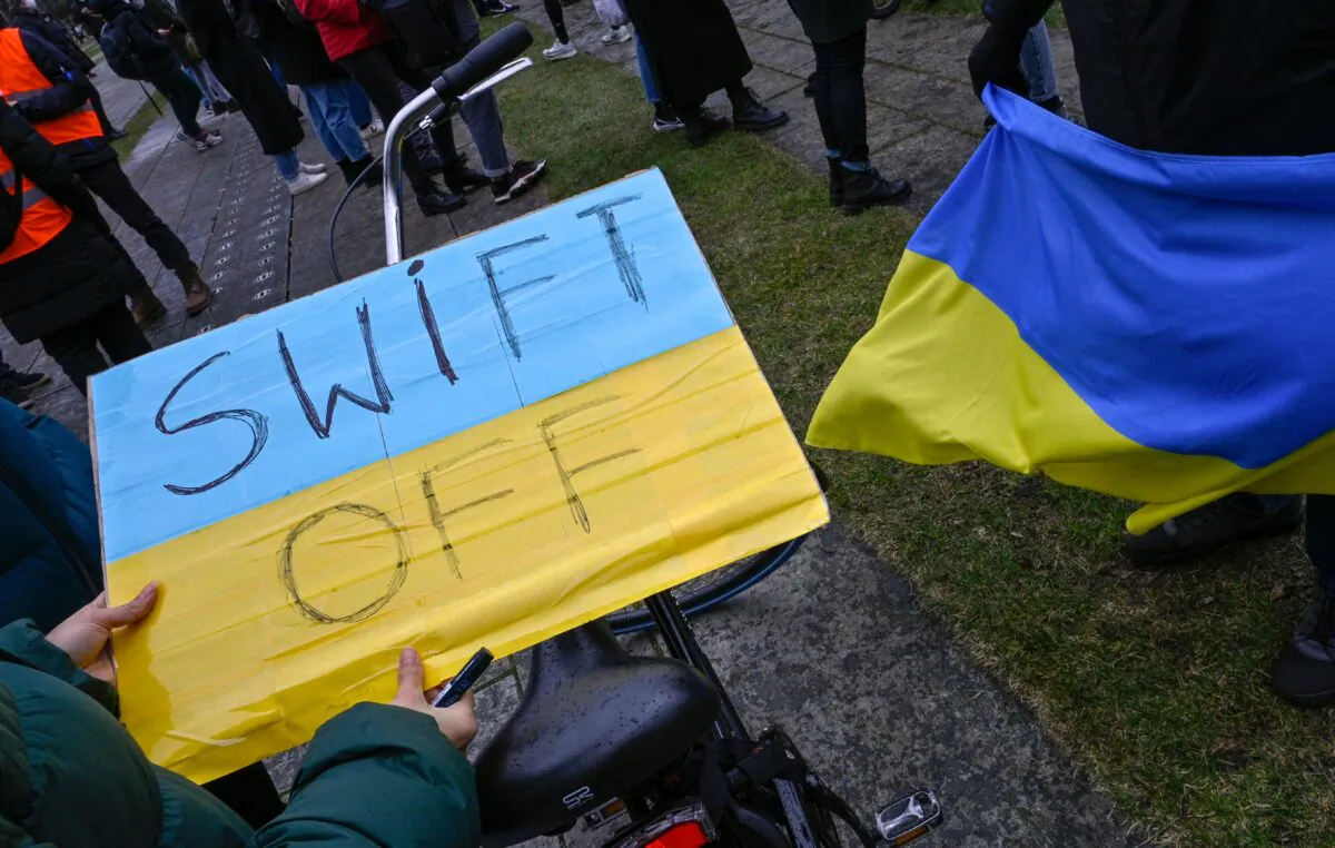 A demonstrator holds a placard reading "SWIFT OFF," referring to the SWIFT interbank payment system, in Berlin, Germany, on Feb. 25, 2022. (John Macdougall/AFP via Getty Images)