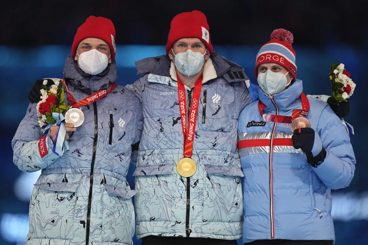 Gold medalist for the men's weather-shortened 50km mass start free cross-country skiing competition, Alexander Bolshunov, centre, of the Russian Olympic Committee stands with compatriot and silver medalist, Ivan Yakimushkin (L) and bronze medalist Simen Hegstad Krueger (R) of Norway on the podium during the closing ceremony of the 2022 Winter Olympics in Beijing, Feb. 20, 2022. (Jae C. Hong/AP Photo)