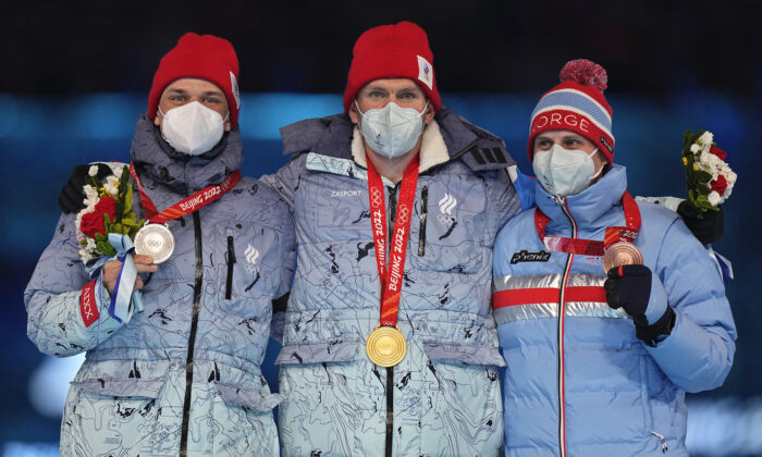 Gold medalist for the men's weather-shortened 50km mass start free cross-country skiing competition, Alexander Bolshunov, centre, of the Russian Olympic Committee stands with compatriot and silver medalist, Ivan Yakimushkin (L) and bronze medalist Simen Hegstad Krueger (R) of Norway on the podium during the closing ceremony of the 2022 Winter Olympics in Beijing, Feb. 20, 2022. (Jae C. Hong/AP Photo)