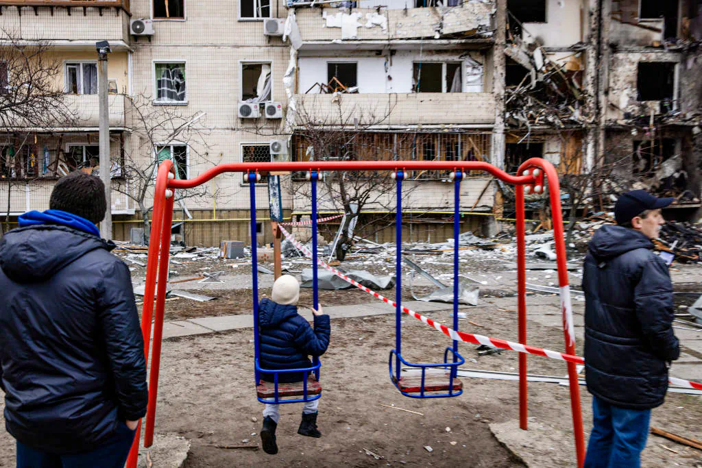 A boy plays on a swing in front of a damaged residential block hit by an early morning missile strike in Kyiv, Ukraine, on Feb. 25, 2022. (Chris McGrath/Getty Images)
